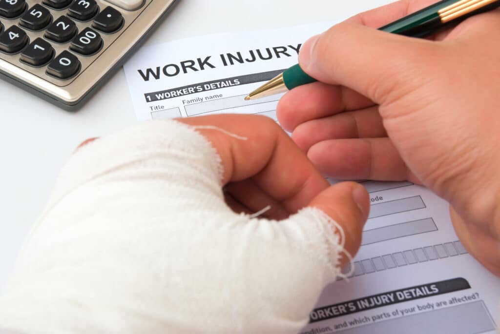 A person with a bandaged hand fills out a workplace injury report